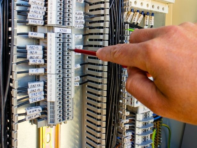 Detail inspeksi teknisi otomasi industri pada instalasi wiring dan terminal block panel kontrol PLC.