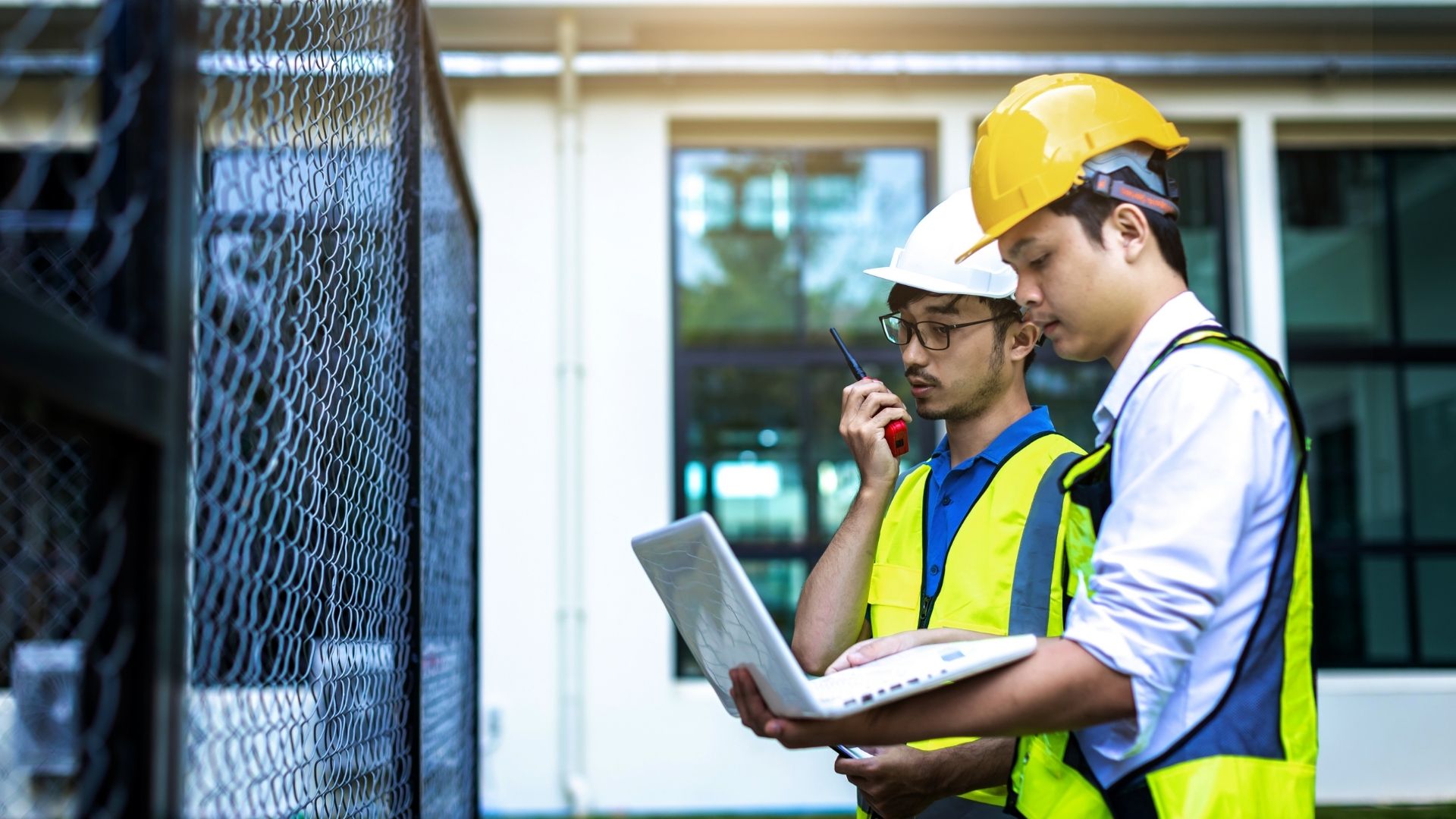 Dua engineer ahli dari ICI Automation sedang melakukan studi kelayakan dan peninjauan arsitektur sistem otomasi industri menggunakan laptop di lokasi proyek.