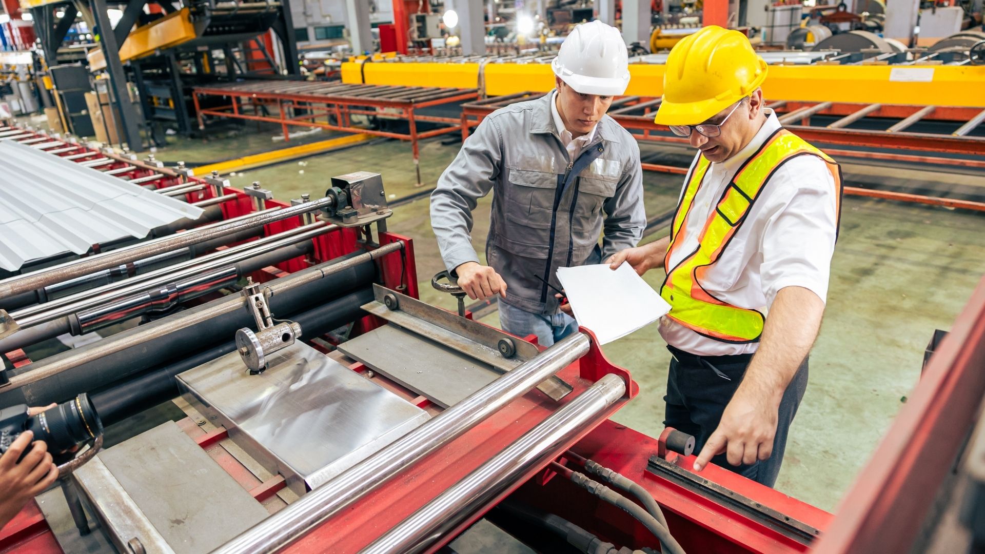 Lead expert dan engineer dari PT Industrial Control Indonesia dengan APD lengkap sedang berdiskusi meninjau dokumen teknis proyek otomasi langsung di lantai produksi fasilitas klien.